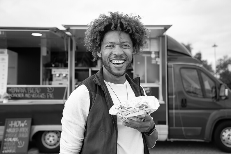 Joyful black man with sandwich standing against food truck